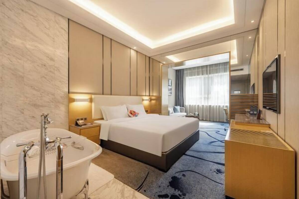 Una habitación de hotel moderna con una cama grande, un baño separado con bañera, un escritorio y una televisión.