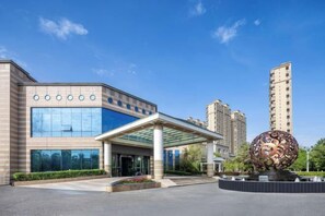 Un edificio moderno con fachada de vidrio, un acceso cubierto y una llamativa escultura esférica al frente.