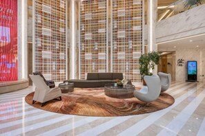 A spacious lobby with a central seating area, a large digital display, and a high ceiling with a grid-like pattern.