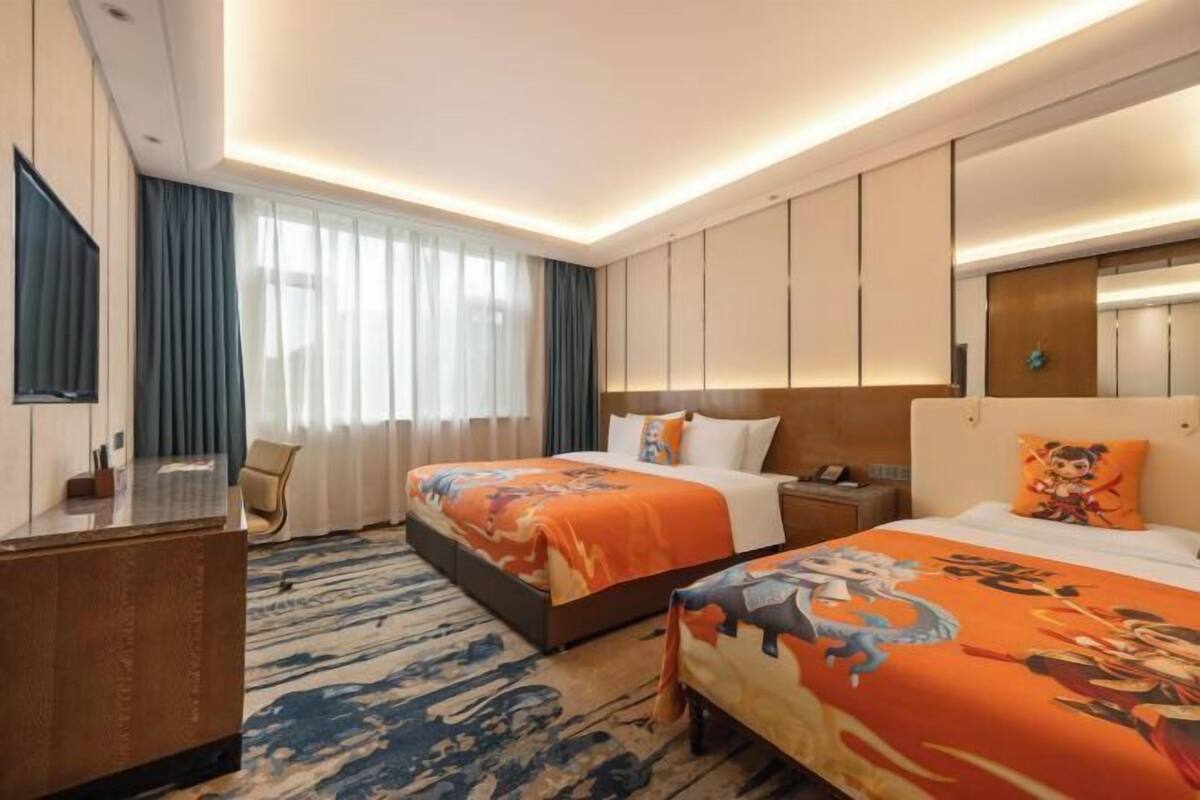 Habitación de hotel con dos camas, un escritorio, una silla y un ventanal con cortinas.