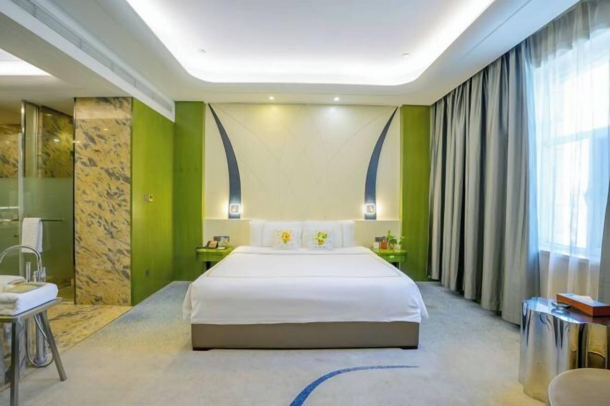 Habitación de hotel con una cama grande, una mesita de noche, un espejo y una ventana con cortinas.