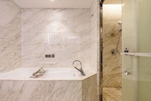 Un baño con pared de mármol, bañera y cabina de ducha con mampara de vidrio.