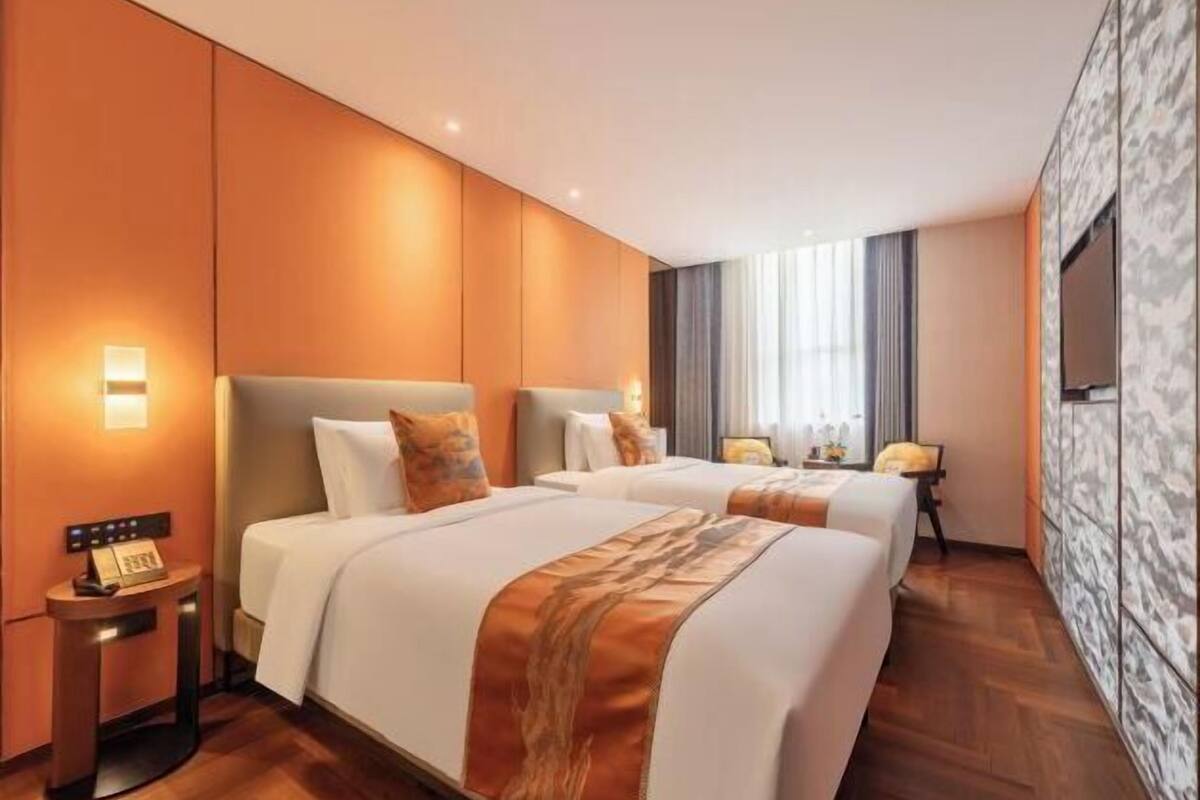 Habitación de hotel con dos camas, un televisor, una mesita de noche con teléfono y una ventana con cortinas.