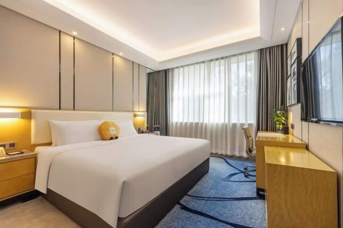 Una habitación de hotel con una cama grande, mesitas de noche, un escritorio, una silla y una ventana con cortinas.