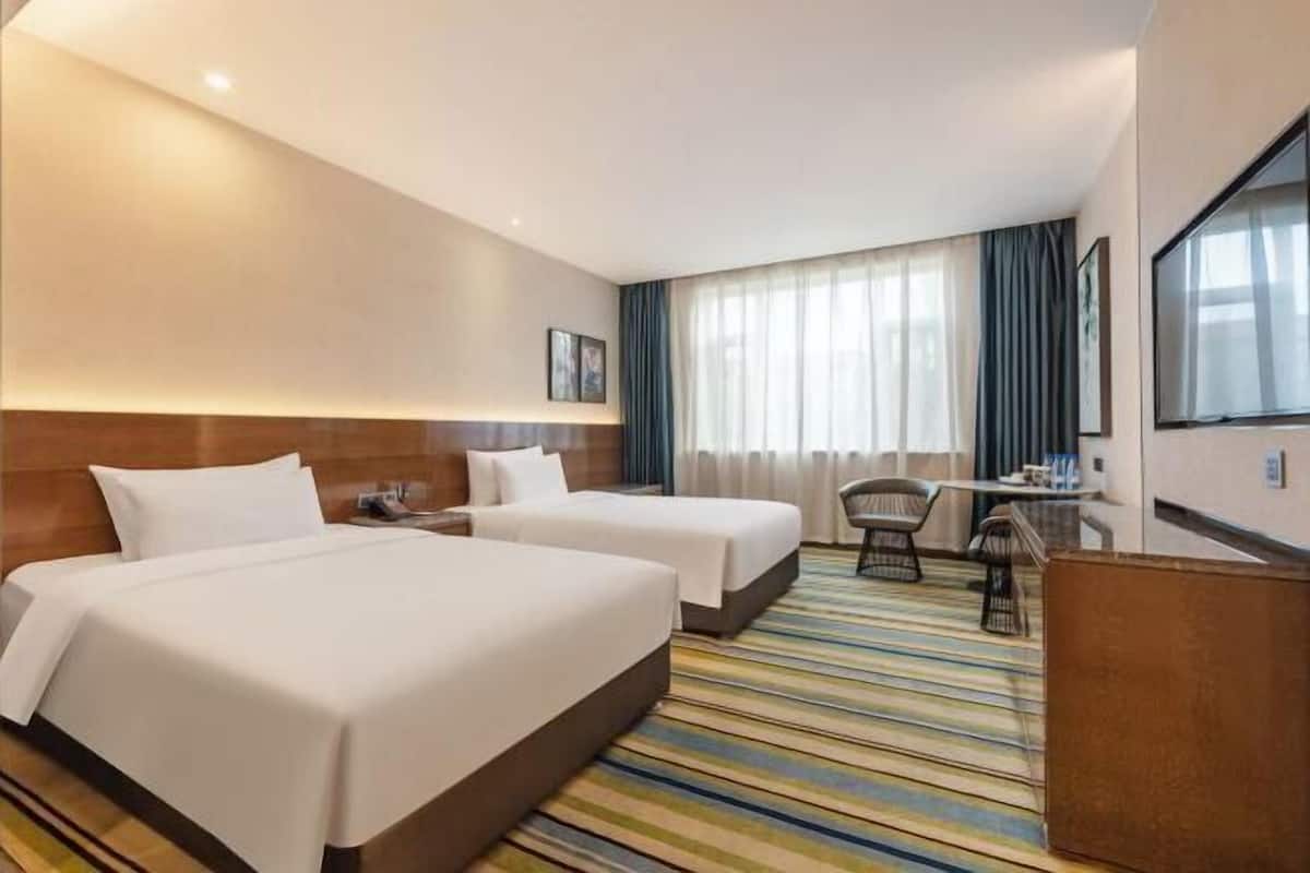 Habitación de hotel con dos camas, un escritorio, una silla, un televisor y una ventana con cortinas.