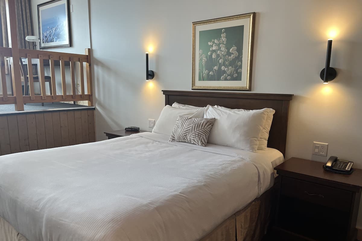 A neatly made bed with white linens, a wooden headboard, and two bedside tables with a phone and a lamp.