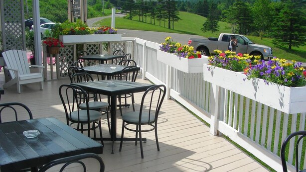 A deck with tables and chairs, surrounded by a white fence and flower planters. - Hôtel Motel La Côte Surprise (Perce)