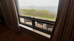 A room with a large window overlooking a wooden deck and a view of the sea. - Hôtel Motel La Côte Surprise (Perce)