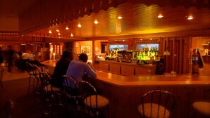 A bar area with wooden decor, bar stools, and a counter with various bottles. - Hôtel Motel La Côte Surprise (Perce)