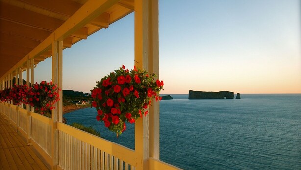 A covered balcony with wooden railings and hanging flower baskets. - Hôtel Motel La Côte Surprise (Perce)