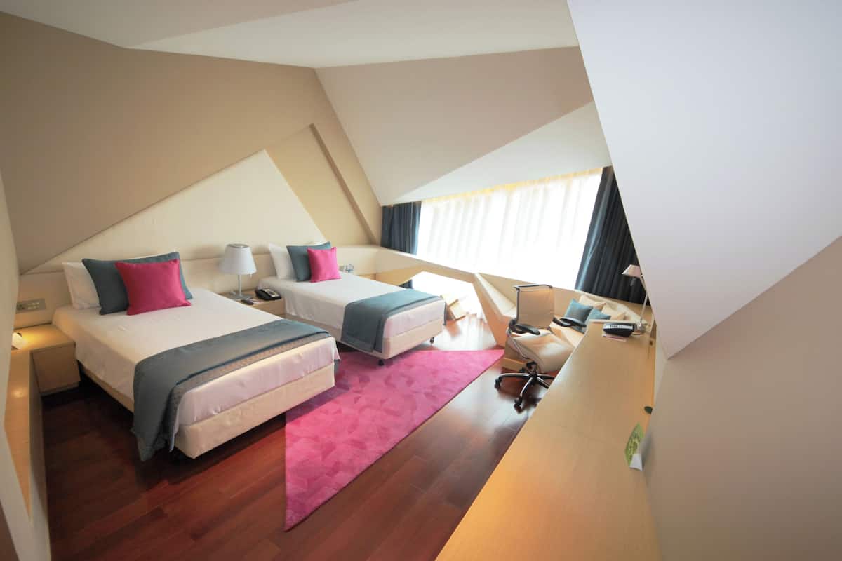 A hotel room with two beds, a desk, a chair, and a large window.