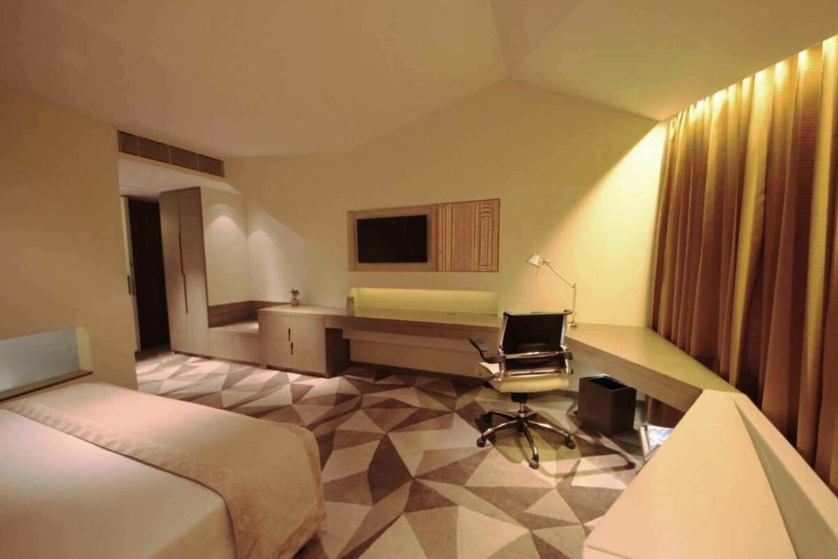 A hotel room with a bed, a desk, a chair, a television, and a lamp.
