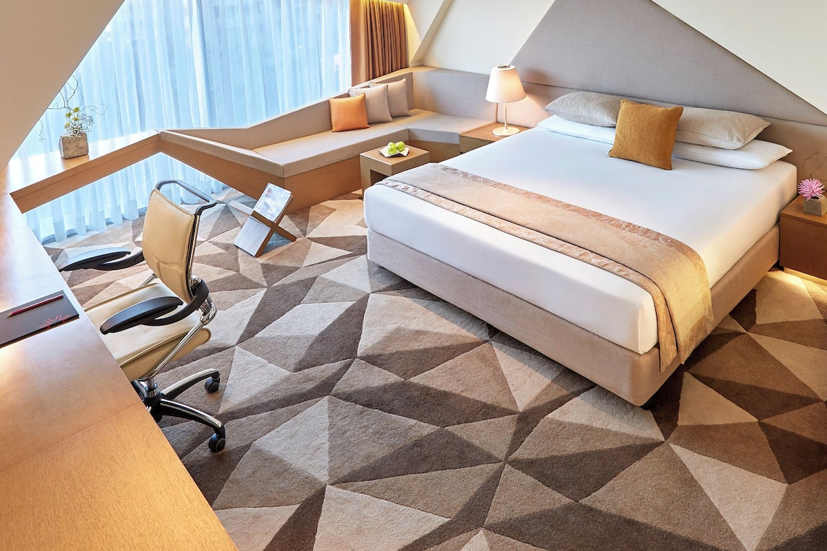 A modern hotel room with a large bed, a desk, and a seating area.