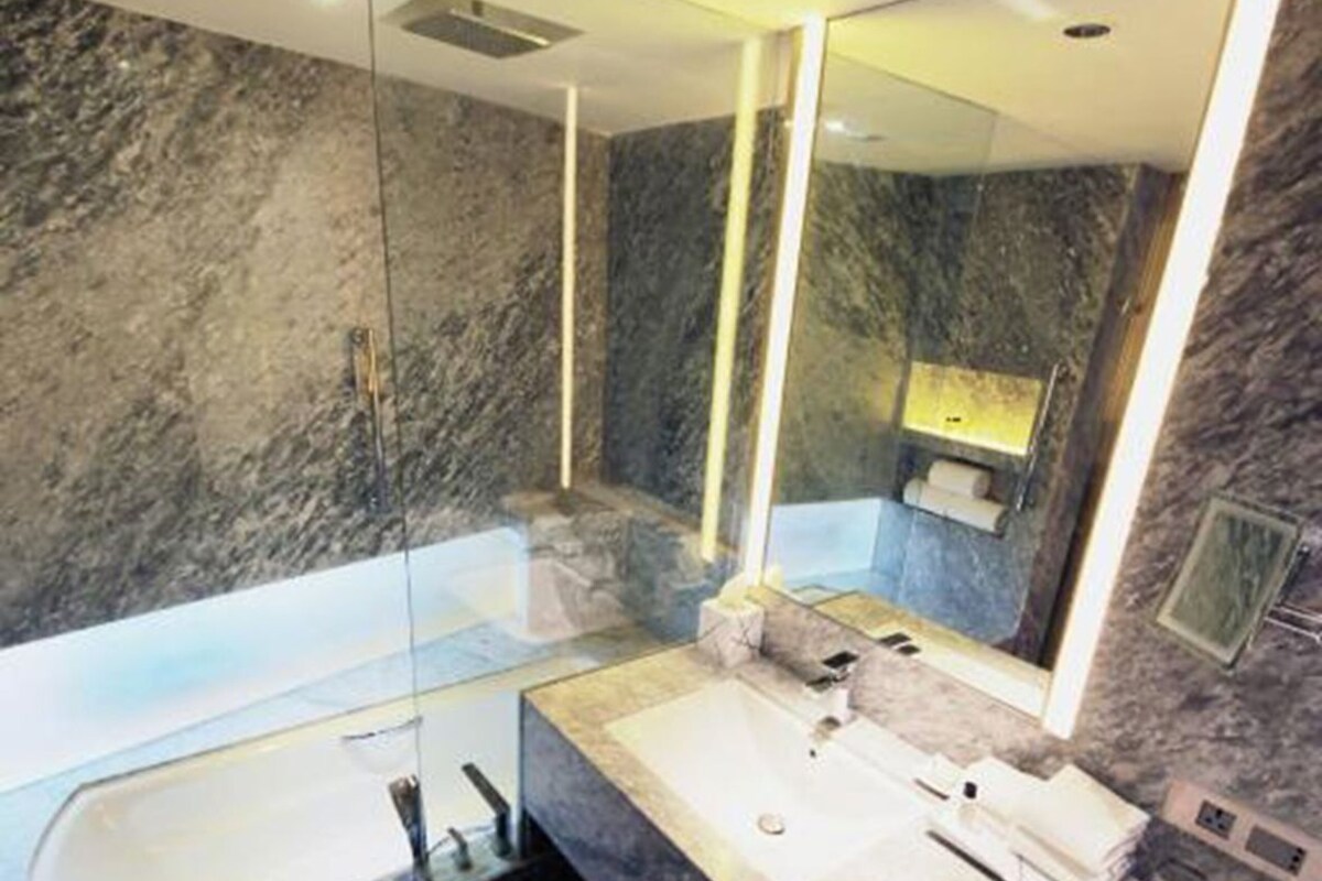 A modern bathroom with a large mirror, a bathtub, and a sink.