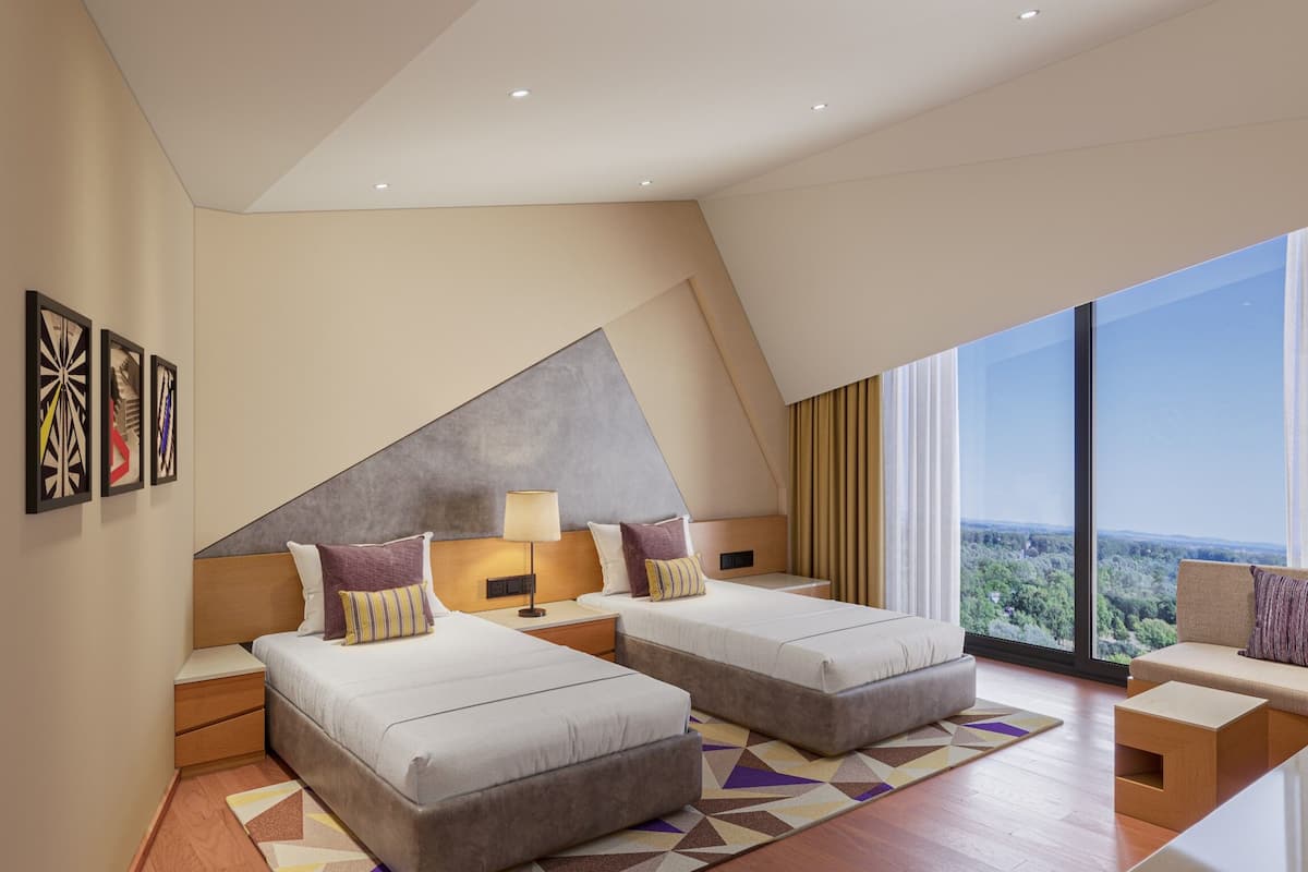A modern hotel room with two beds, a sofa, and a large window offering a view of the landscape.