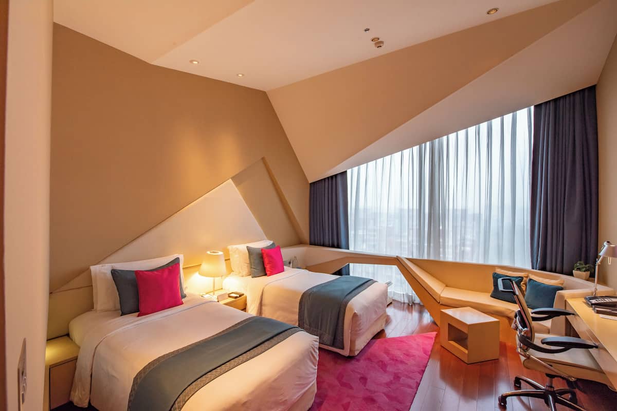 A modern hotel room with two beds, a desk, and a chair.