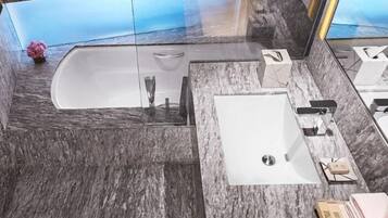 Un baño moderno con piso de mármol, una bañera, un lavamanos y un espejo grande.