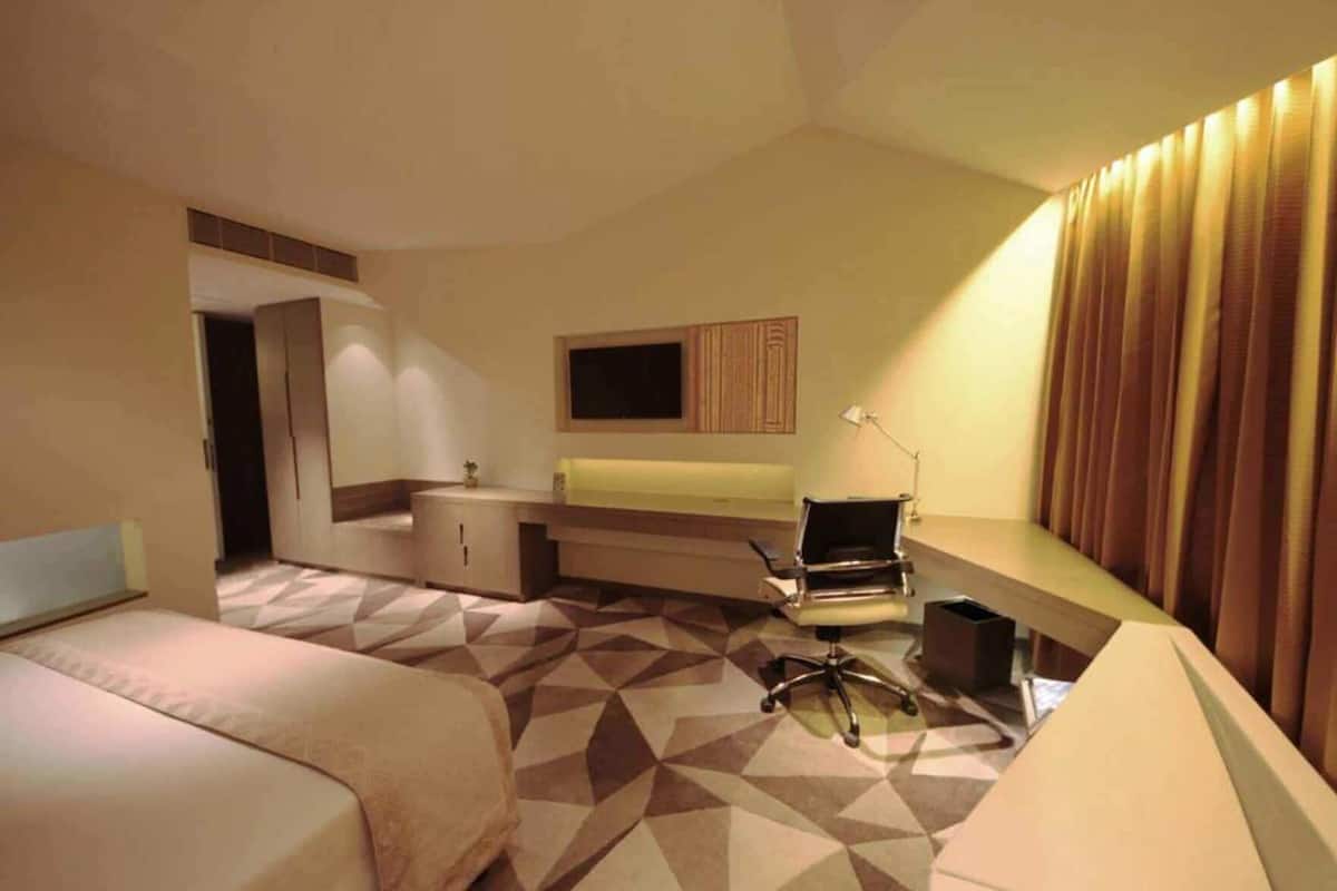 A hotel room with a bed, a desk, a chair, a television, and a lamp.