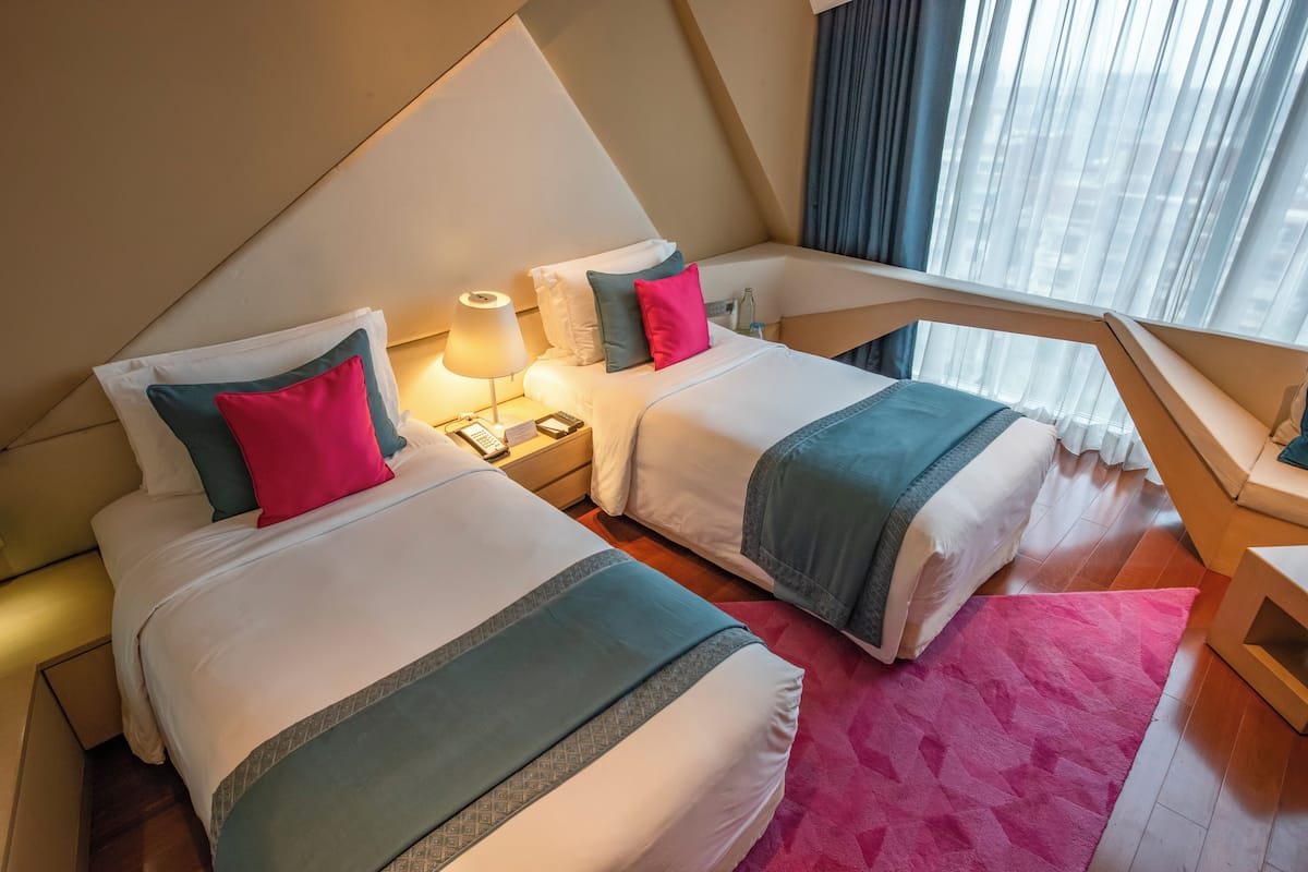 A hotel room with two beds, each with a pillow and a bedside table with a lamp.