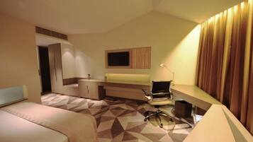 A hotel room with a bed, a desk with a chair, a television, and a window with curtains.