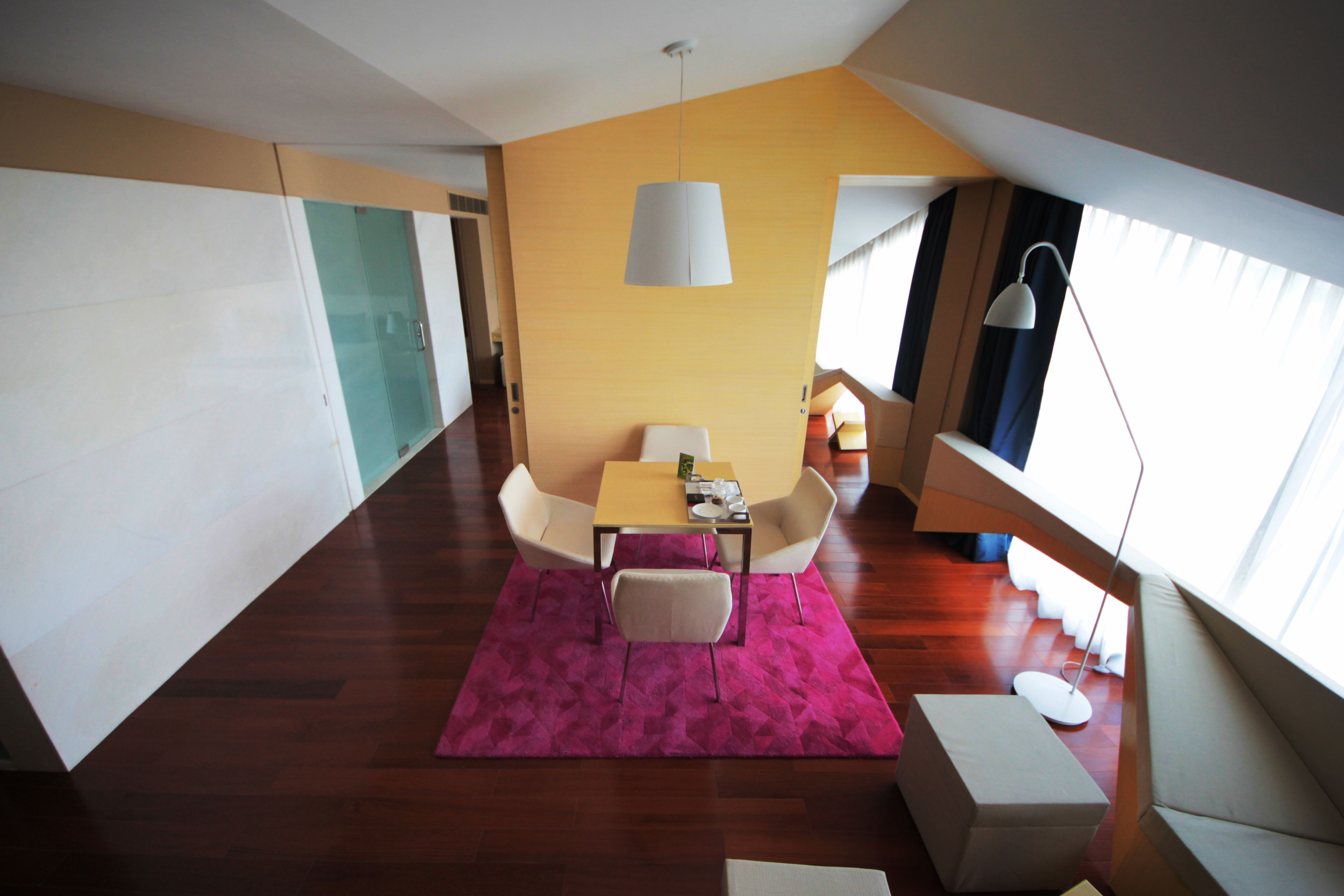 A modern dining area with a table and chairs, a pink rug, and a large window with curtains.