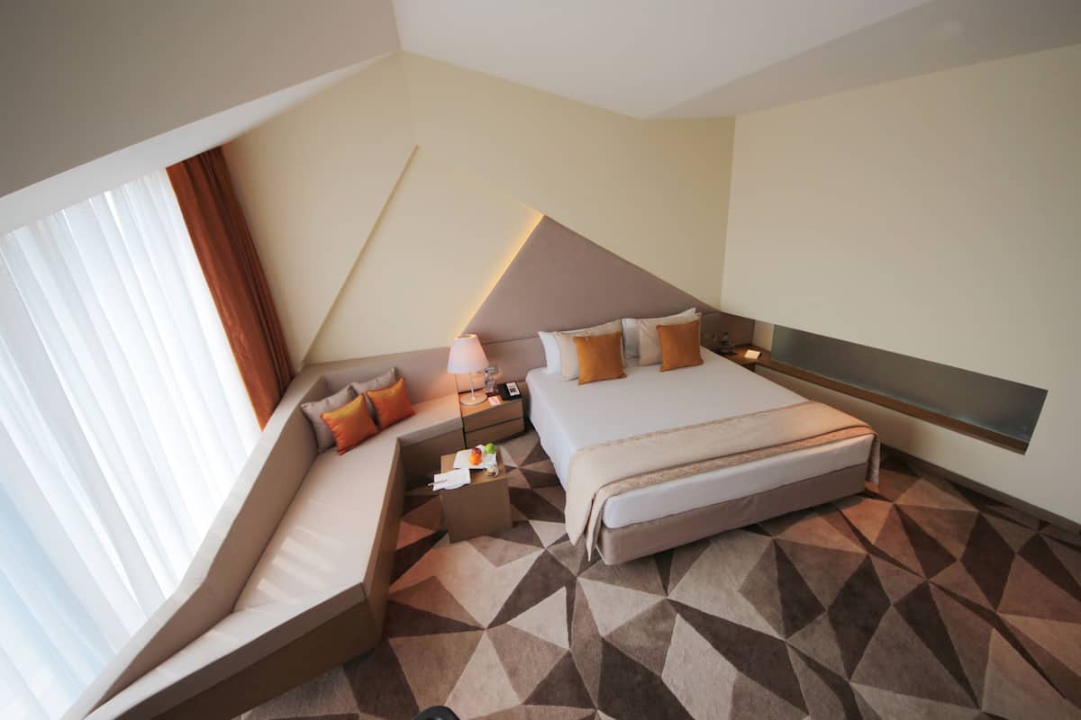 A modern hotel room with a bed, a sofa, a desk, and a large window with curtains.