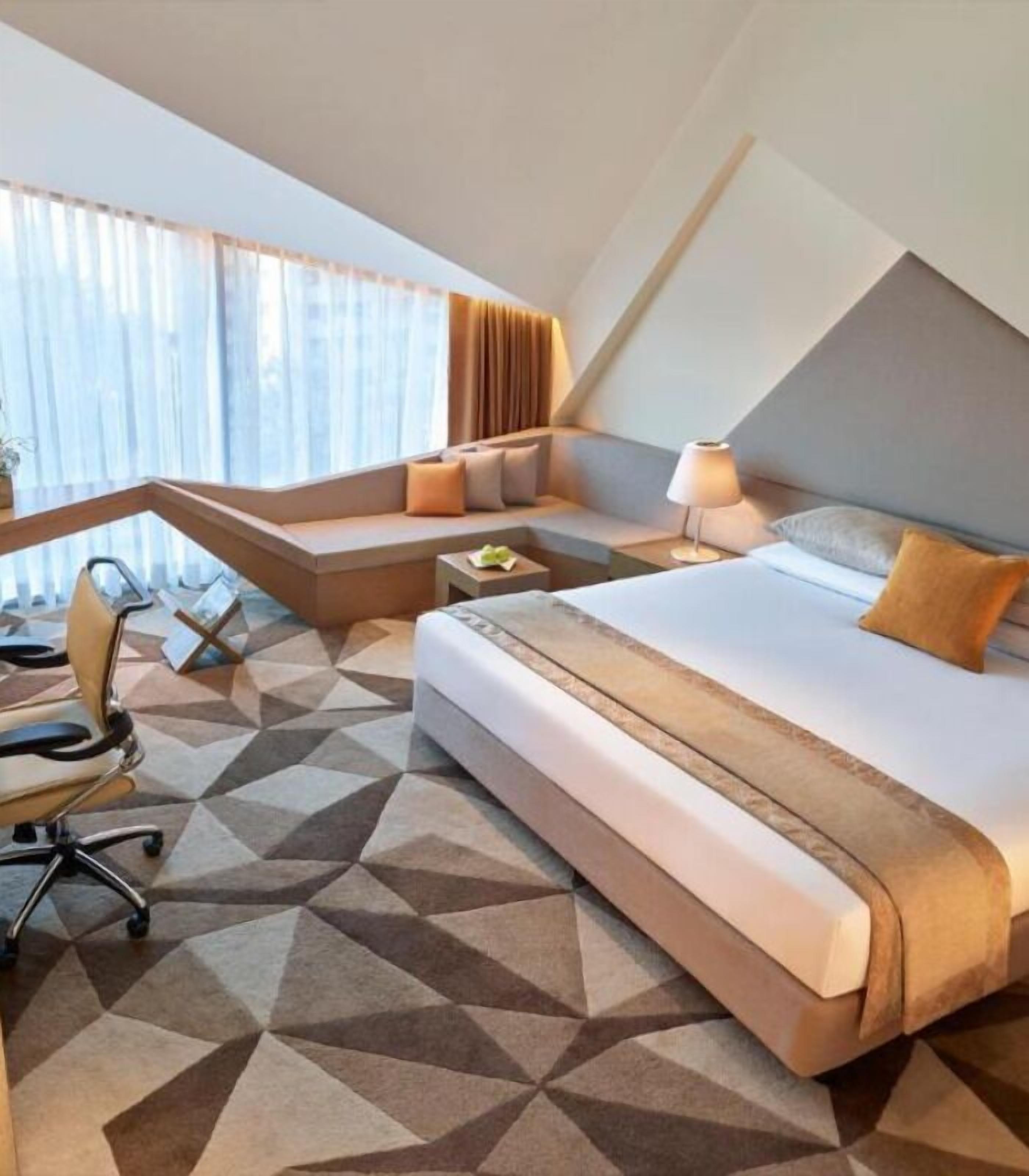 A modern hotel room with a large bed, a desk, and a chair.