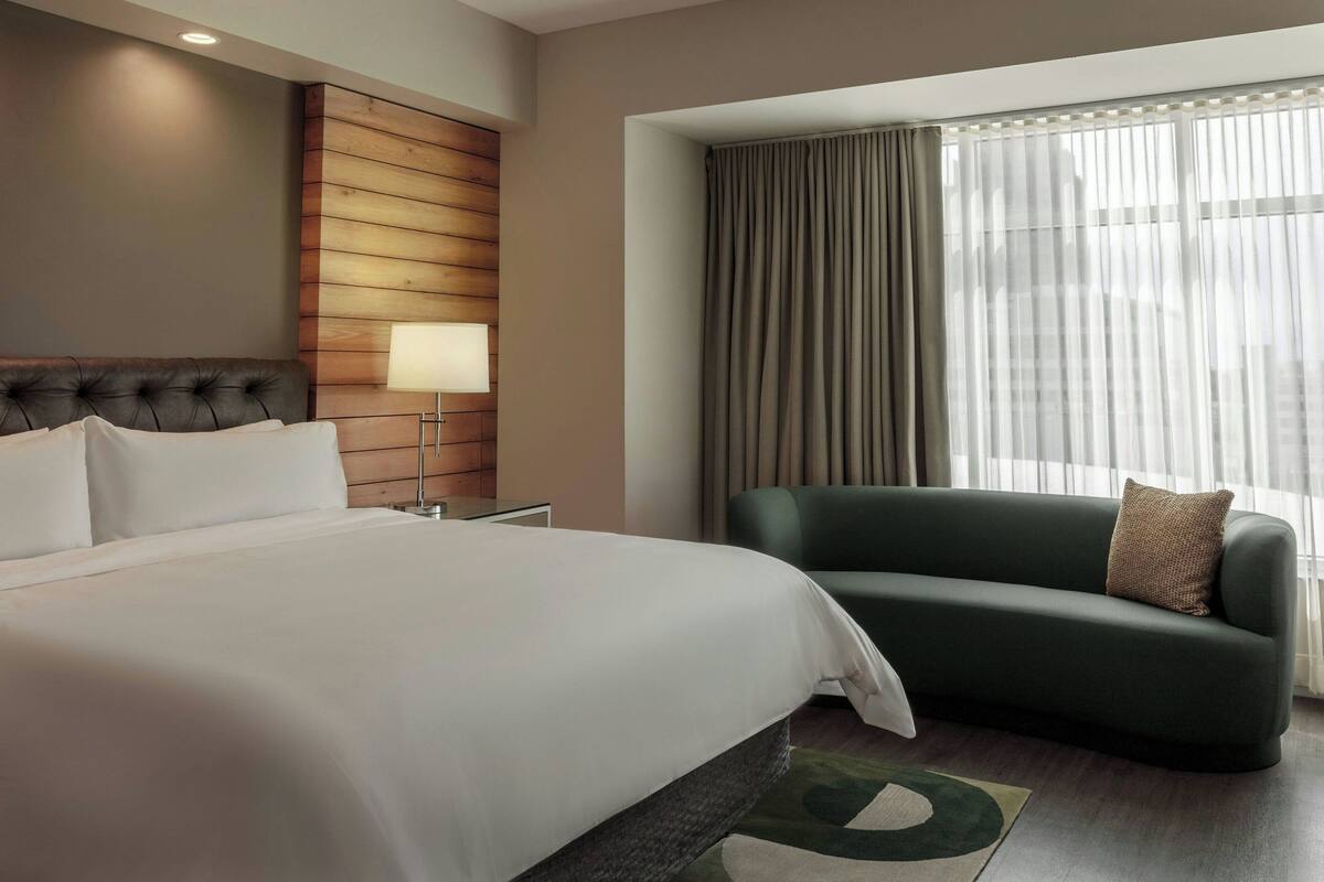 A hotel room with a large bed, a green sofa, a lamp, and a window with curtains.