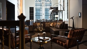 Un salon moderne avec un canapé, des fauteuils et une table basse. Il y a une grande fenêtre aux arches et un lustre.