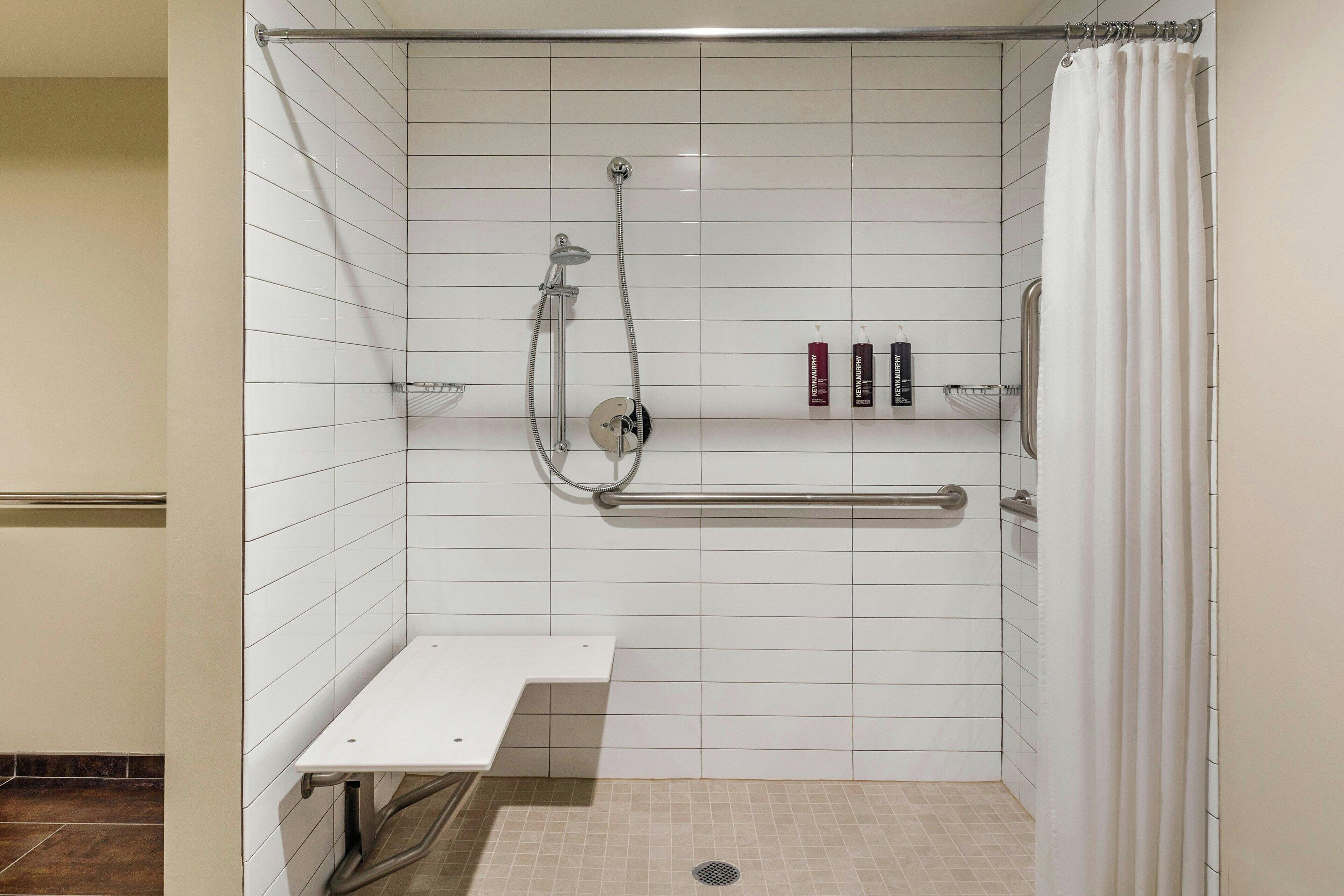 A shower area with white tiles, a grab bar, a shelf with toiletries, and a white bench.