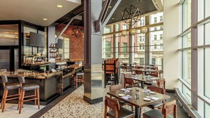Un restaurant moderne doté d’un bar, de hauts plafonds et de grandes fenêtres offrant une vue sur le paysage urbain.
