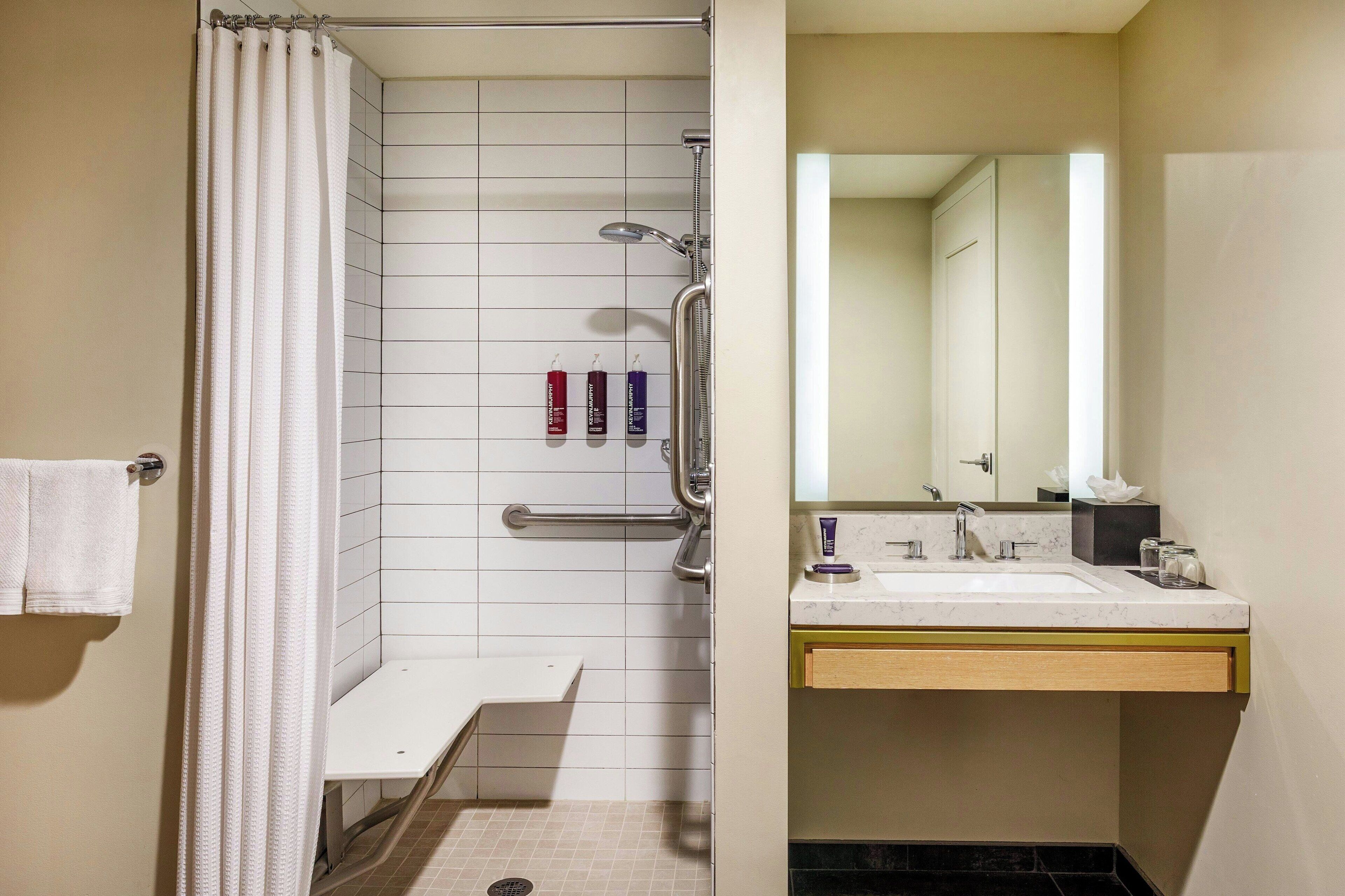 A bathroom with a shower, a sink, and a mirror. There are toiletries on the sink counter.