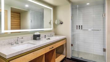 A bathroom with a large mirror, two sinks, a vanity with drawers, and a glass-enclosed shower area.