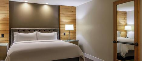 A hotel room with a large bed, wooden panel walls, a mirror, and a nightstand with a lamp.