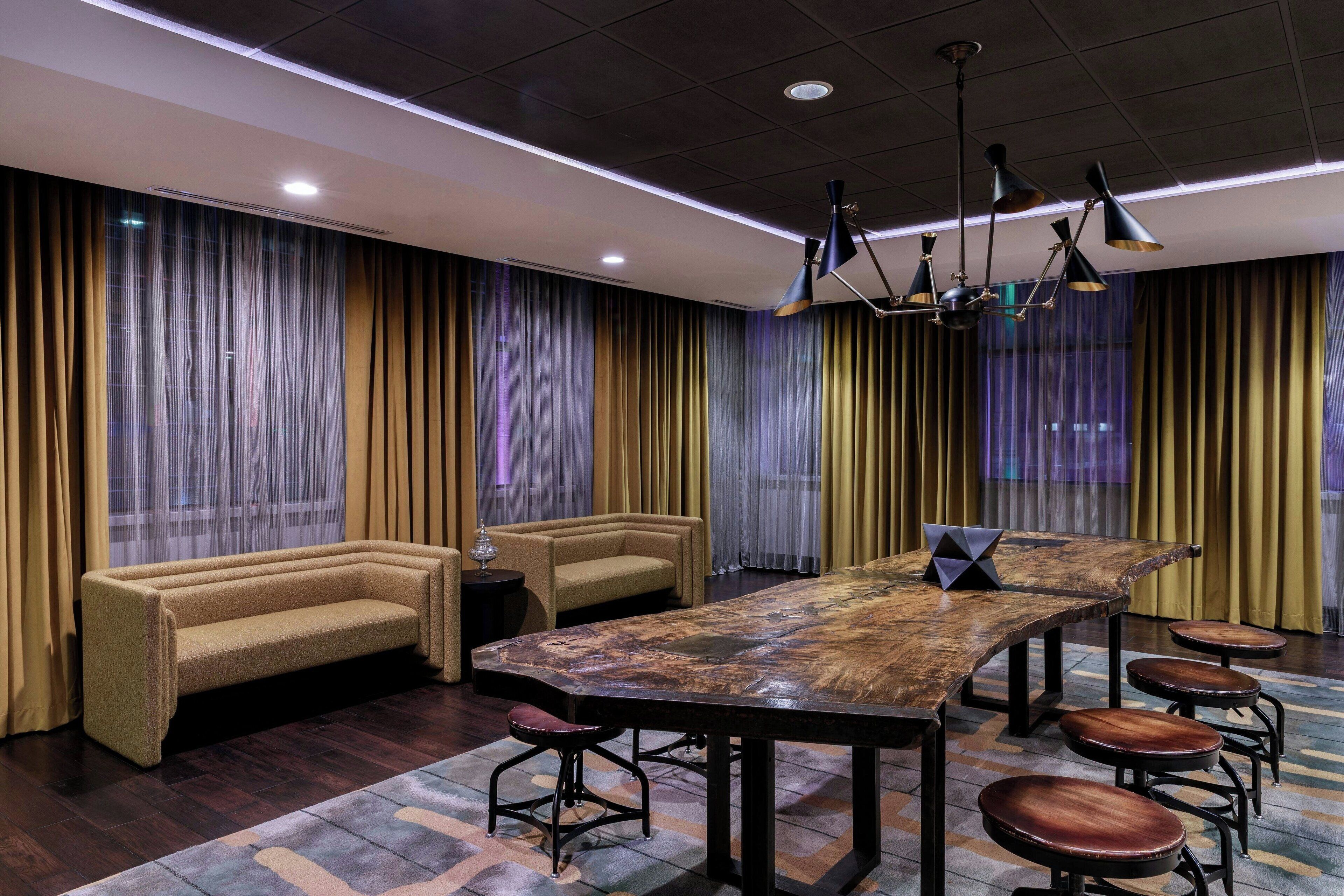 A modern conference room with a long table, four stools, two sofas, and a chandelier.