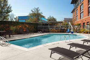 Une piscine rectangulaire à l’eau d’un bleu limpide, entourée de chaises longues et d’une pergola.