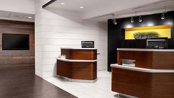 A reception area with two wooden reception desks, a flat-screen TV mounted on the wall, and a potted plant on the right desk.