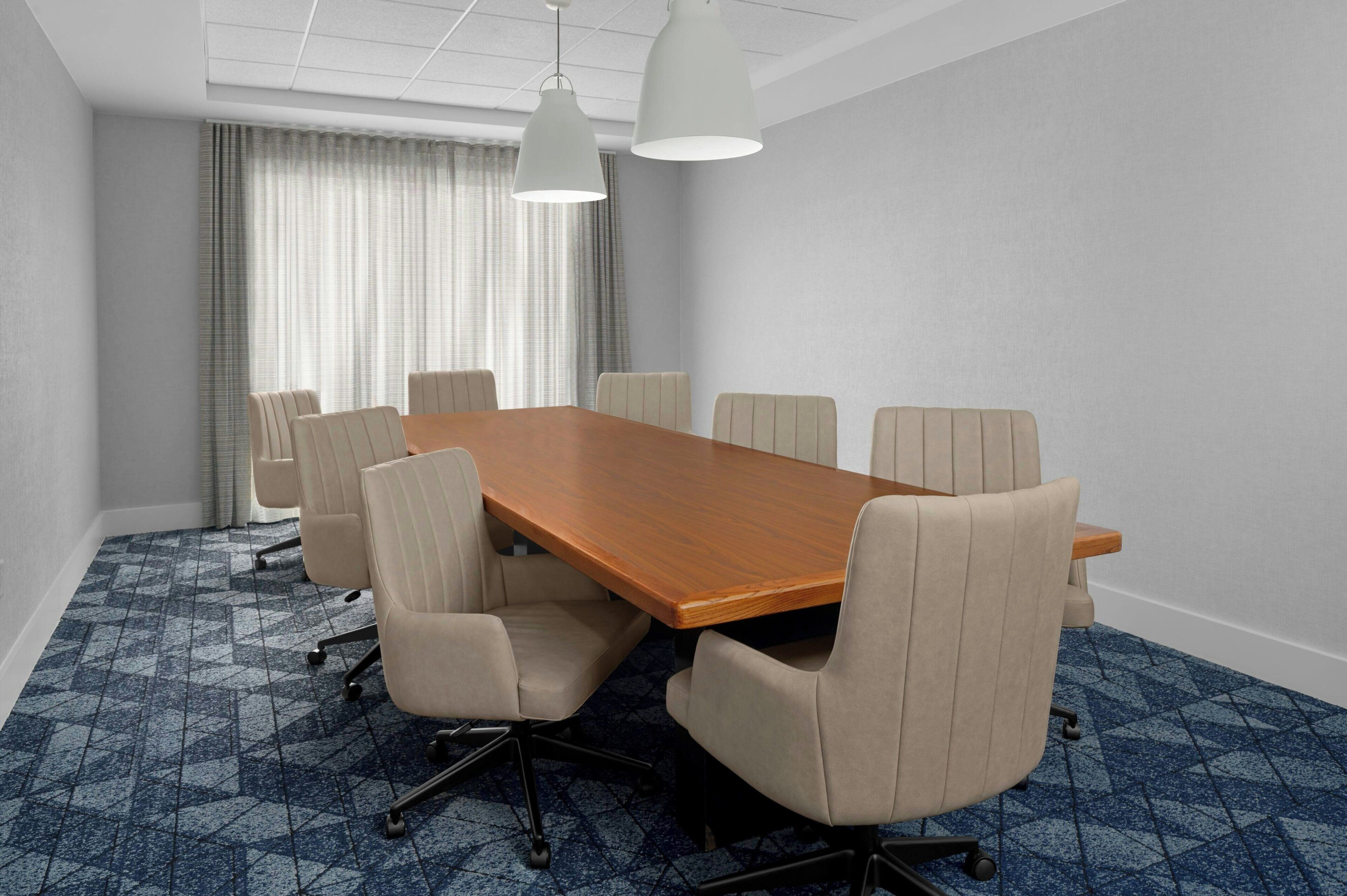 A conference room with a long wooden table, six chairs, and two pendant lights.