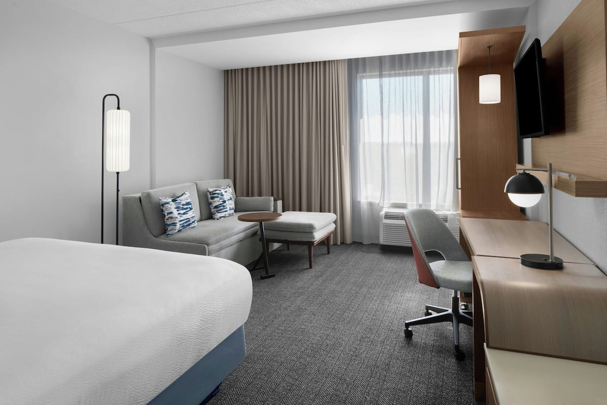 Une chambre d’hôtel équipée d’un lit, d’un bureau, d’une chaise, d’un canapé, d’une télévision et d’une fenêtre avec des rideaux.