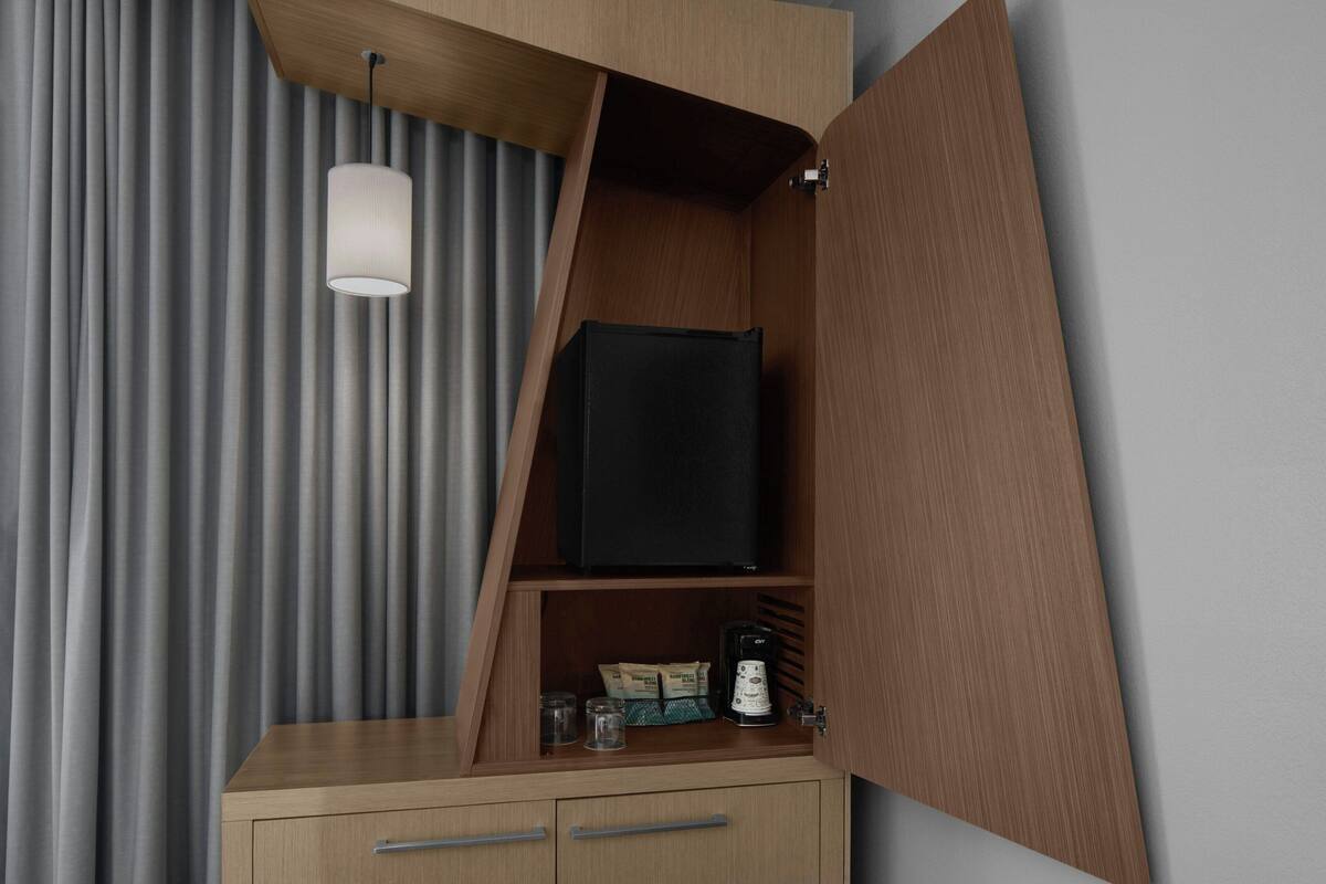 Une chambre compacte et moderne, dotée d’un téléviseur intégré, d’une machine à café et d’un petit meuble avec des tiroirs.