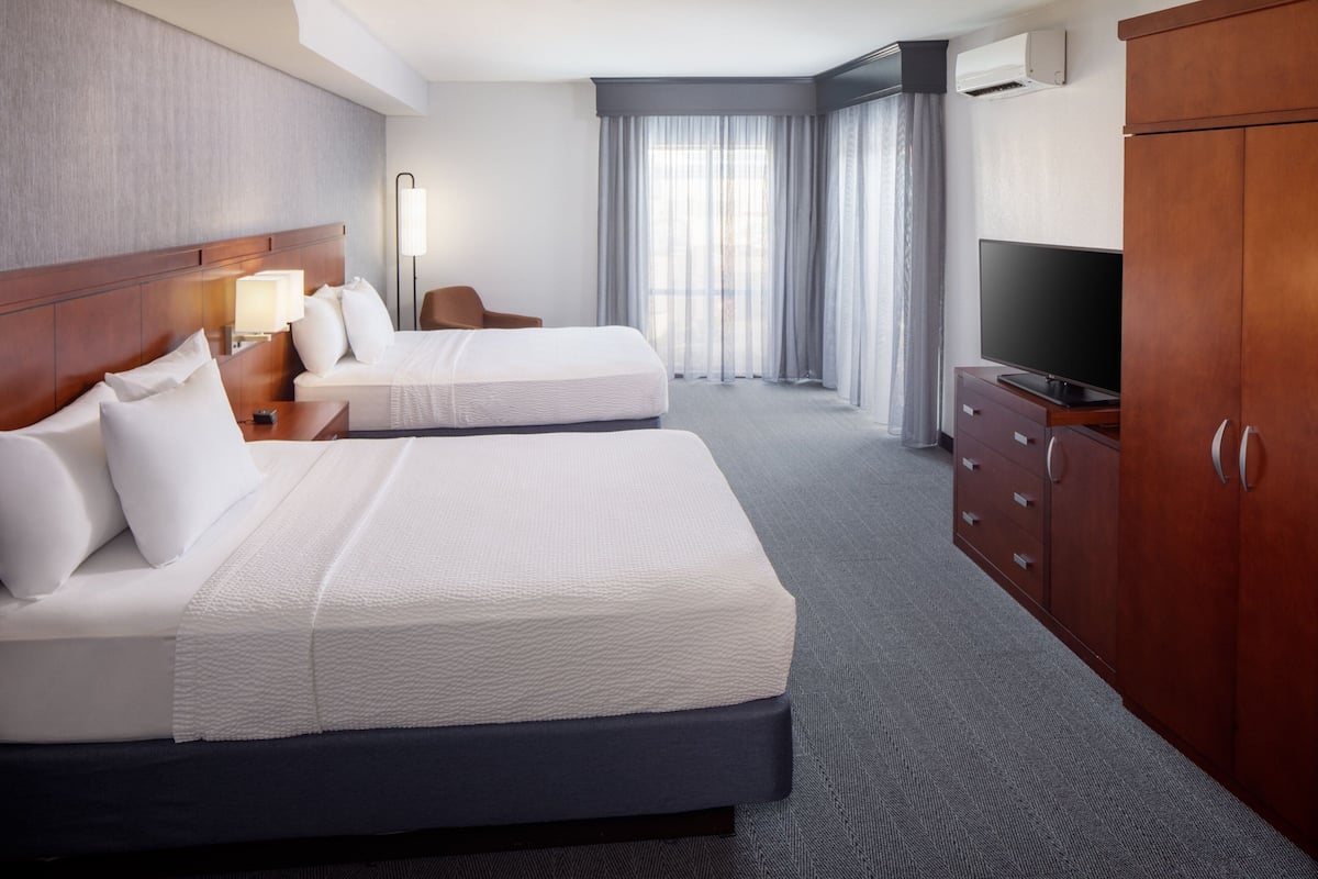 Une chambre d’hôtel avec deux lits, une télévision, une armoire et une grande fenêtre avec des rideaux.