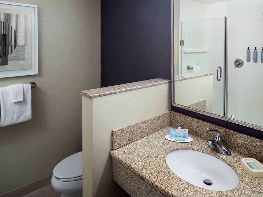 Un baño con lavamanos de encimera de granito, un espejo, toallero y cabina de ducha.