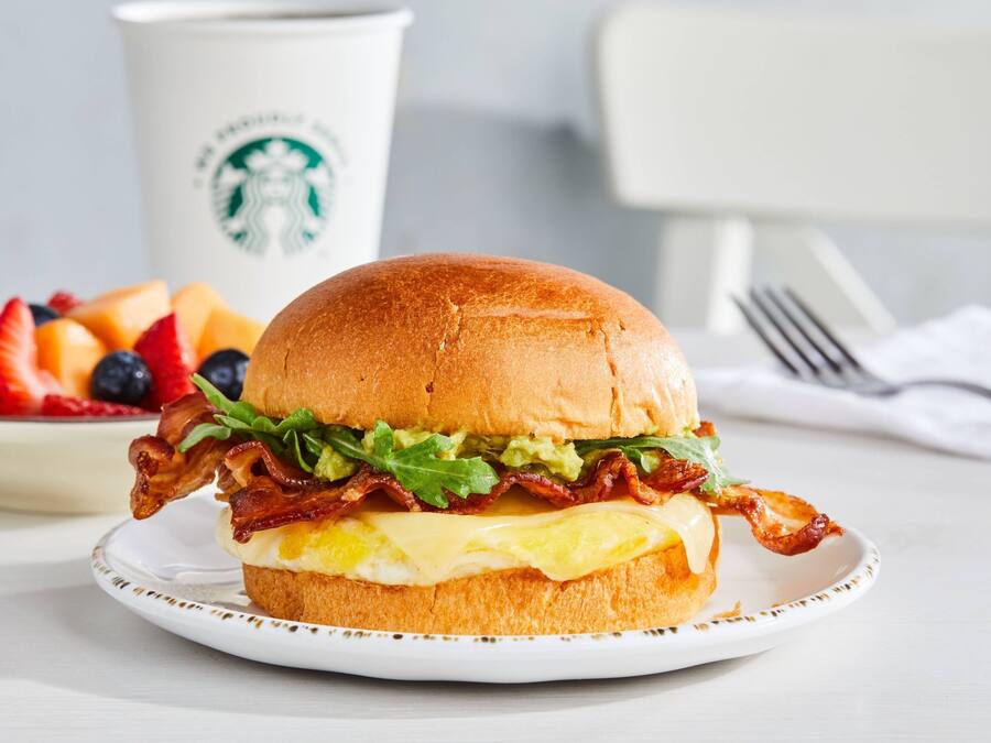 Un sándwich de desayuno en un plato, con una taza y un tenedor al fondo.
