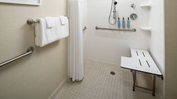 A modern bathroom with a shower, grab bars, a towel rack, and a small table.