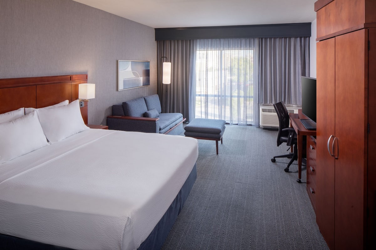 Une chambre d’hôtel avec un grand lit, un bureau, une chaise, un canapé et une armoire.