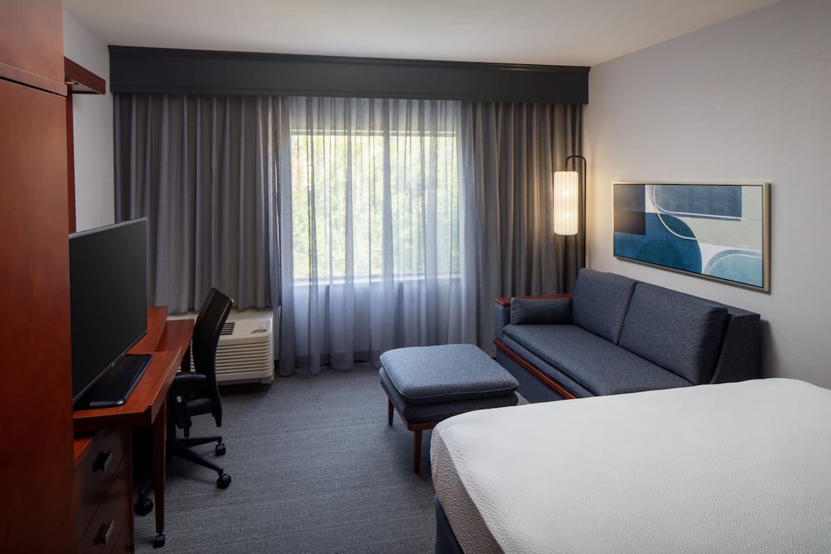 Une chambre d  ’hôtel avec un lit, un bureau équipé d’un ordinateur, un canapé et une grande fenêtre avec des rideaux.
