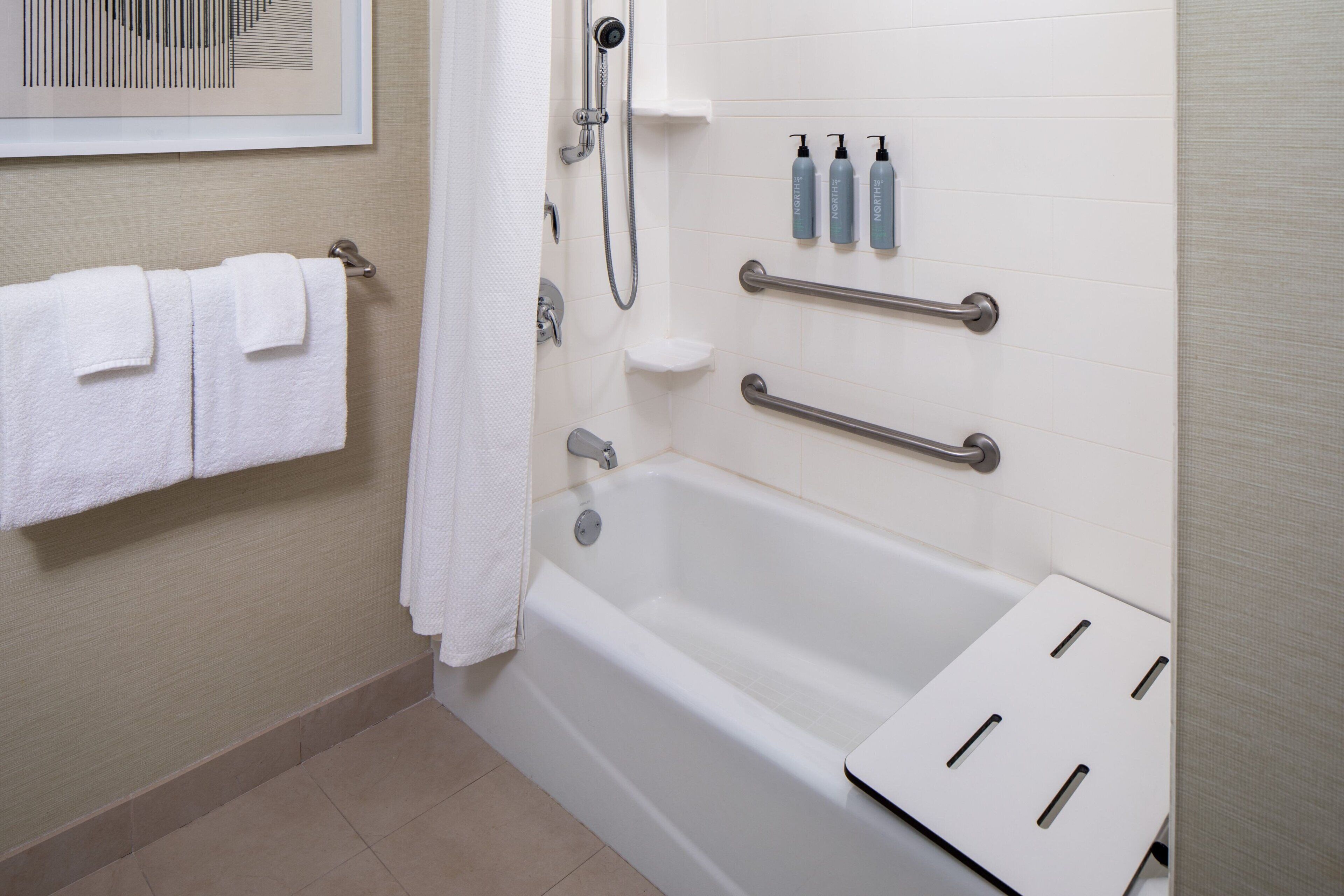 A bathroom with a bathtub, handrails, a towel rack, and toiletries on the wall.