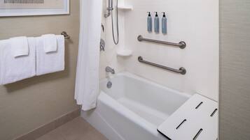 A bathroom with a bathtub, handrails, a towel rack, and toiletries on the wall.