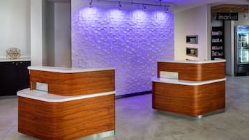 A reception area with two wooden reception desks, a wall with a geometric pattern, and a refrigerator stocked with beverages.