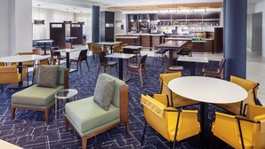 A hotel lobby with seating areas, a bar, and a kitchen in the background.
